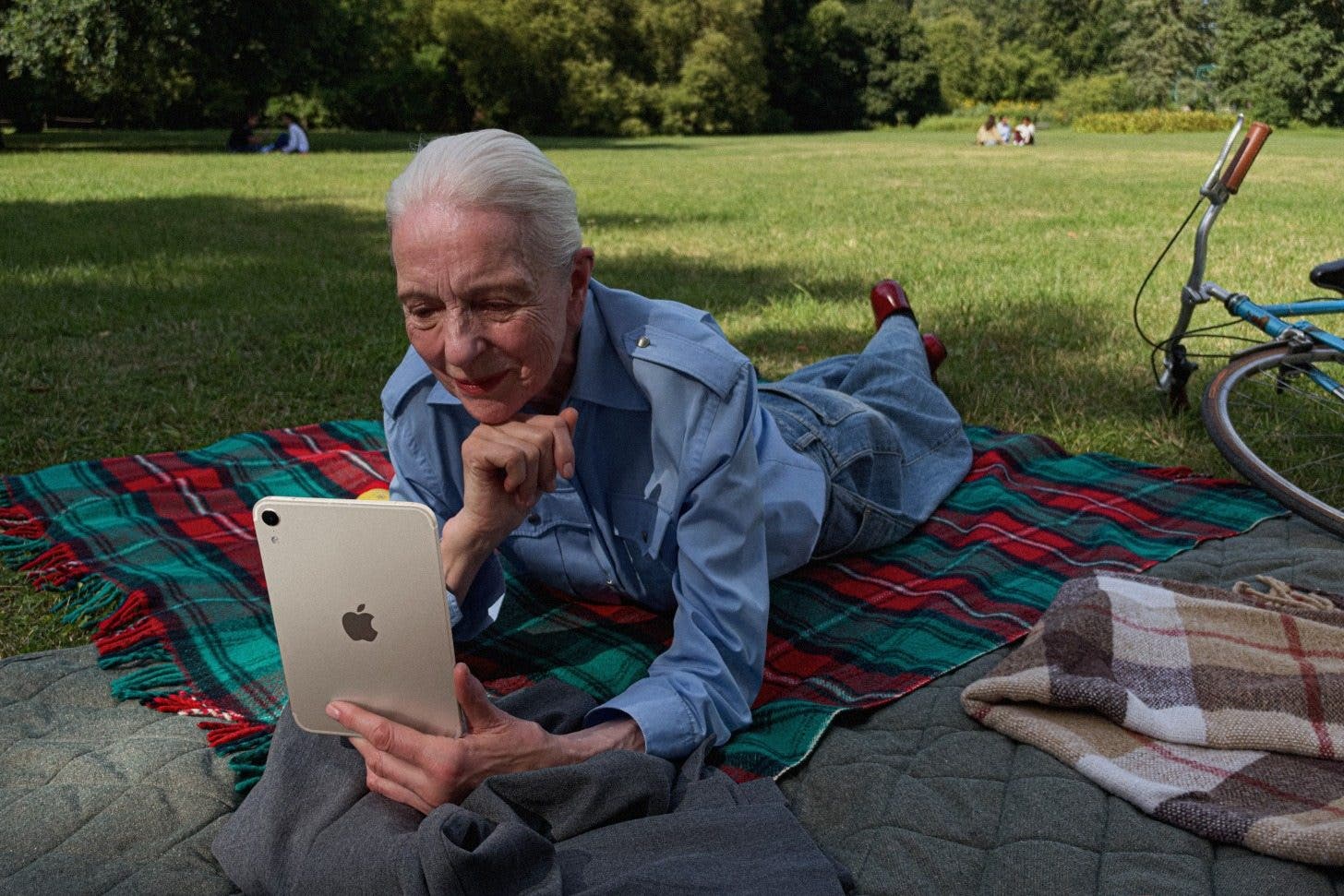 an image of a woman holding an ipad mini while laying on a blanket outside on the grass