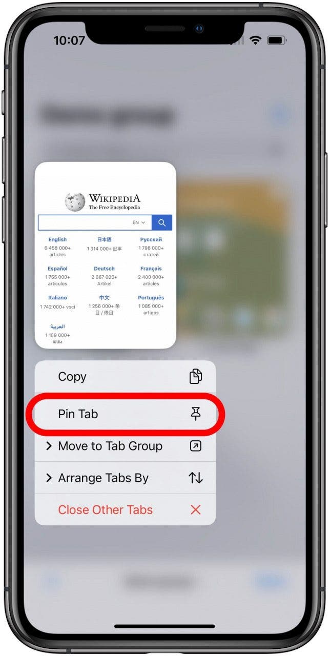 Safari app with the tabs screen for a Tab Group blurred in the background and a single tab visible with the long press menu open below it. The Pin Tab option is marked in the menu.